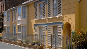 A row of yellow buildings with white shutters, a metal fence, and a brick base.