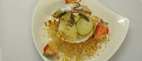 Un plato de postre con una presentación original, que incluye una fresa, una porción de pastel y un adorno con forma de hoja.