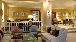 A spacious living area with a high ceiling, a balcony, and a seating arrangement including a sofa, armchairs, and a coffee table. - Wentworth Hotel (Aldeburgh)