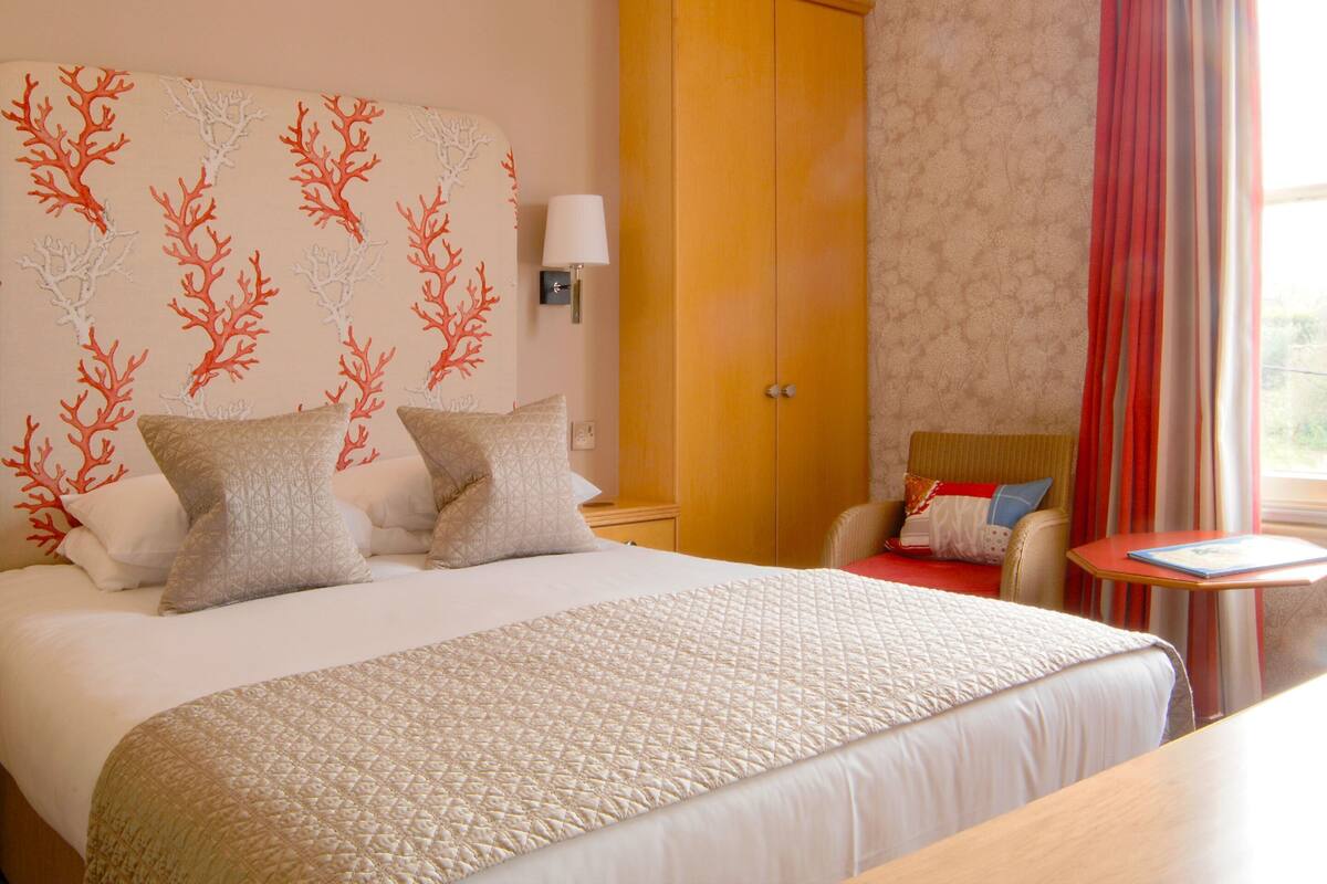 A hotel room with a bed, a wardrobe, a bedside table, and a window with curtains.