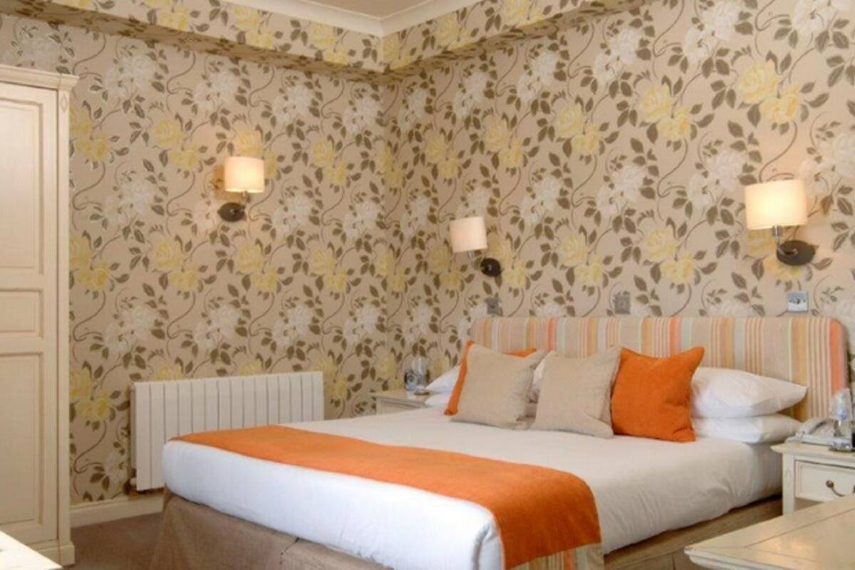 A hotel room with a bed, two bedside tables, a nightstand, a radiator, and floral wallpaper.