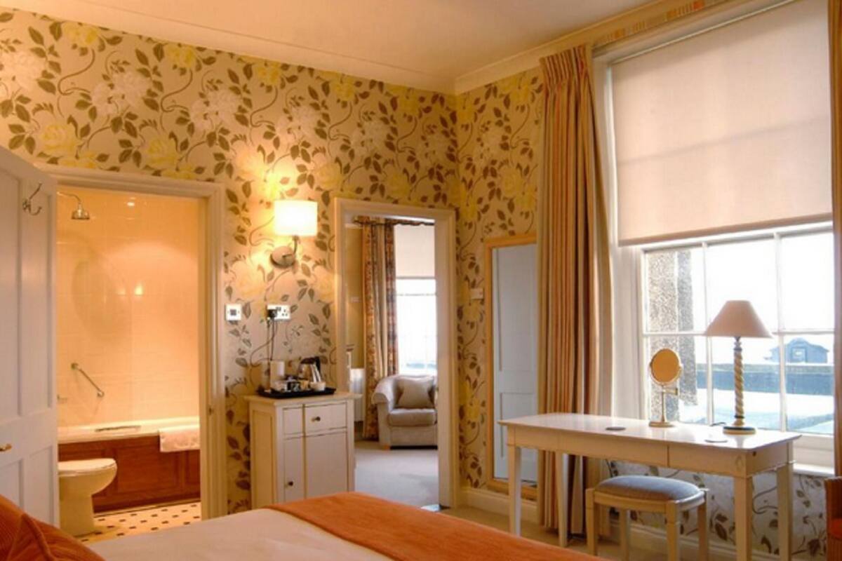 A hotel room with a shower, a desk with a chair, a bed, and a view of the sea through the window.
