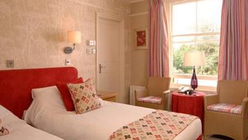 A hotel room with a large bed, two chairs, a small table with a lamp, and a window with curtains.
