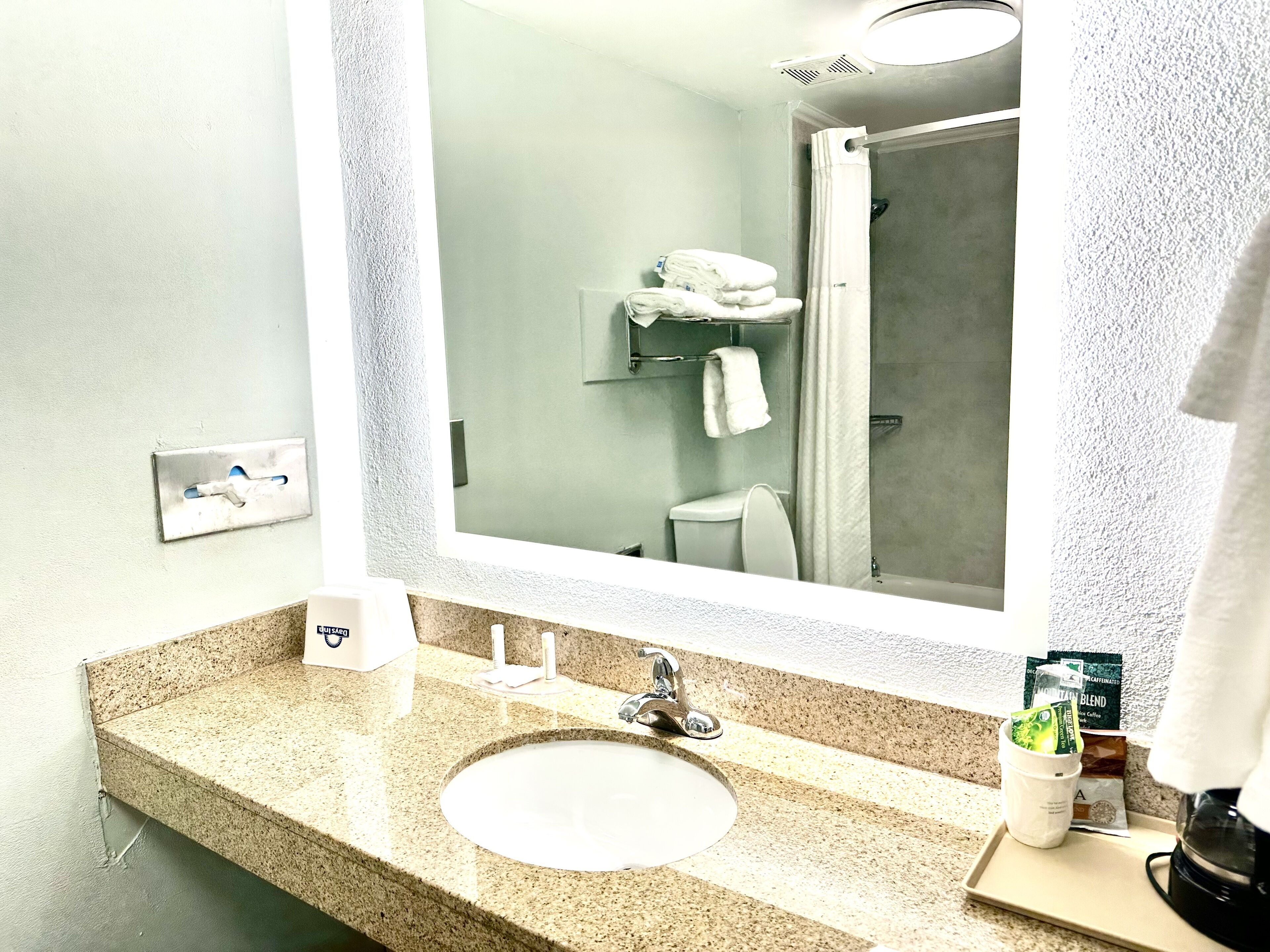 Une salle de bain avec un lavabo surmonté d’un plan de travail en granit, un miroir, une douche et un porte-serviettes.