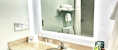 A bathroom with a granite countertop sink, a mirror, a shower, and a towel rack.