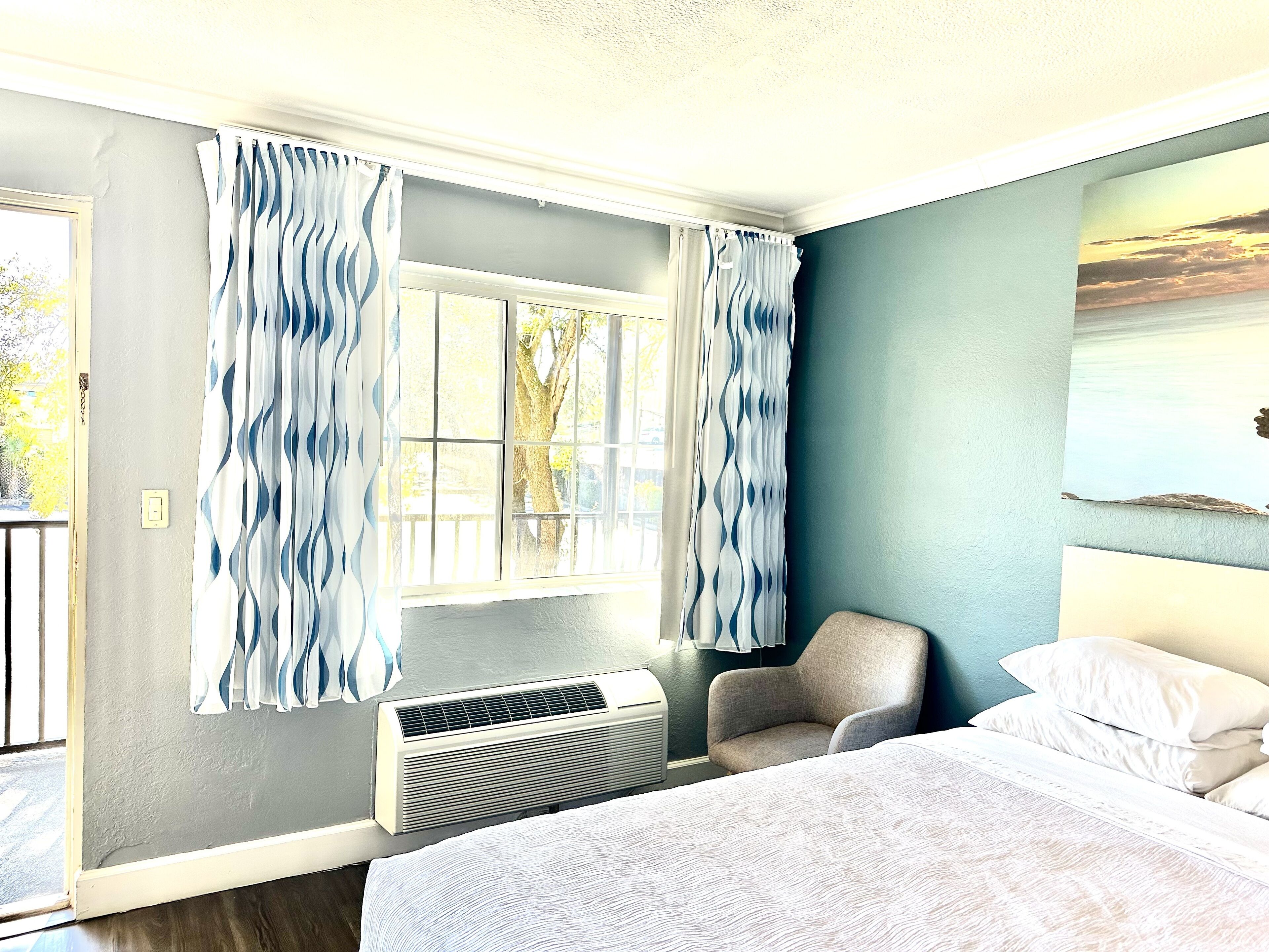 Une chambre d’hôtel équipée d’un lit, d’une chaise, d’une fenêtre avec des rideaux et d’un appareil de climatisation.