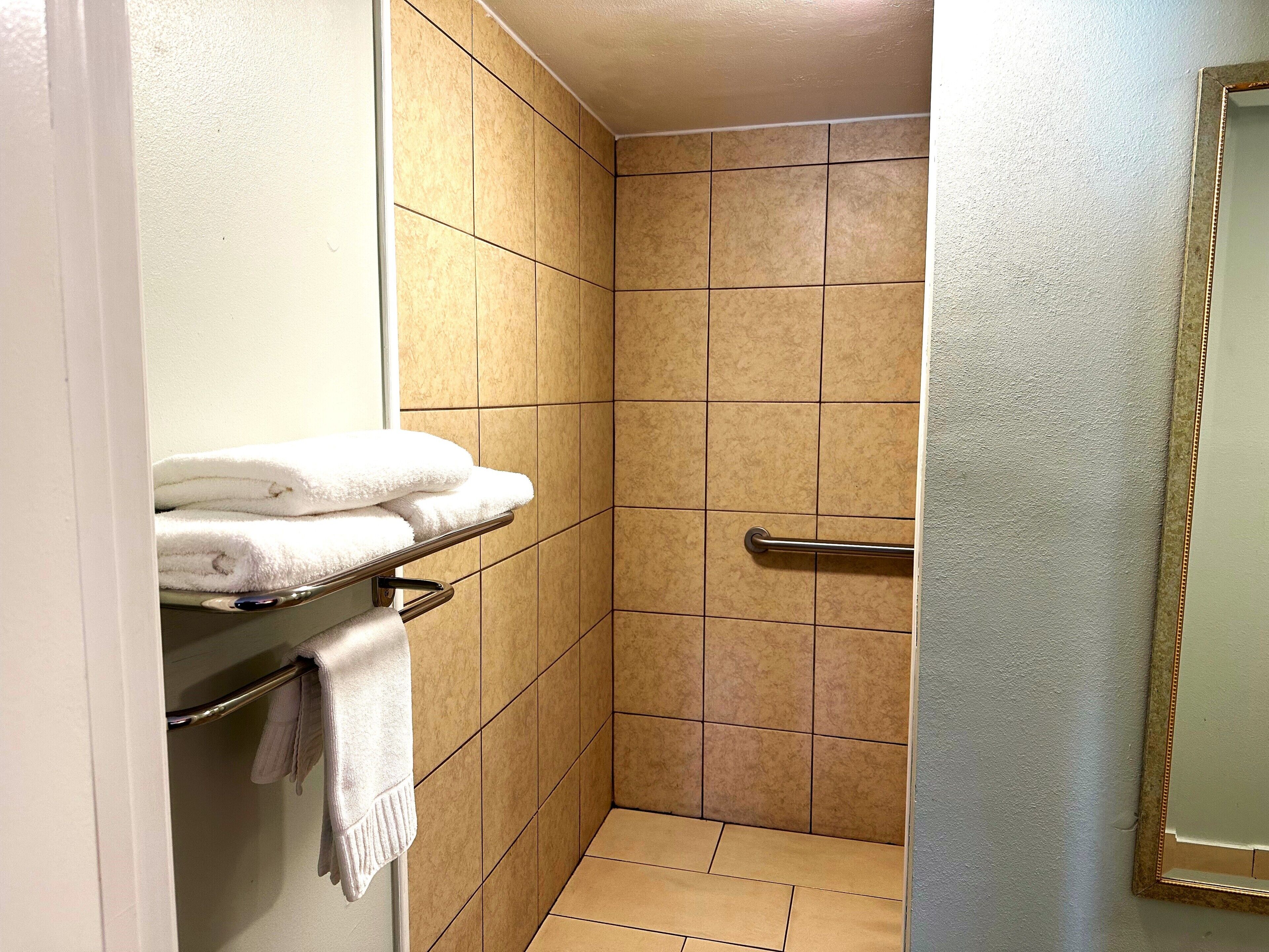 A bathroom with a shower stall, a towel rack with folded towels, and a handrail.
