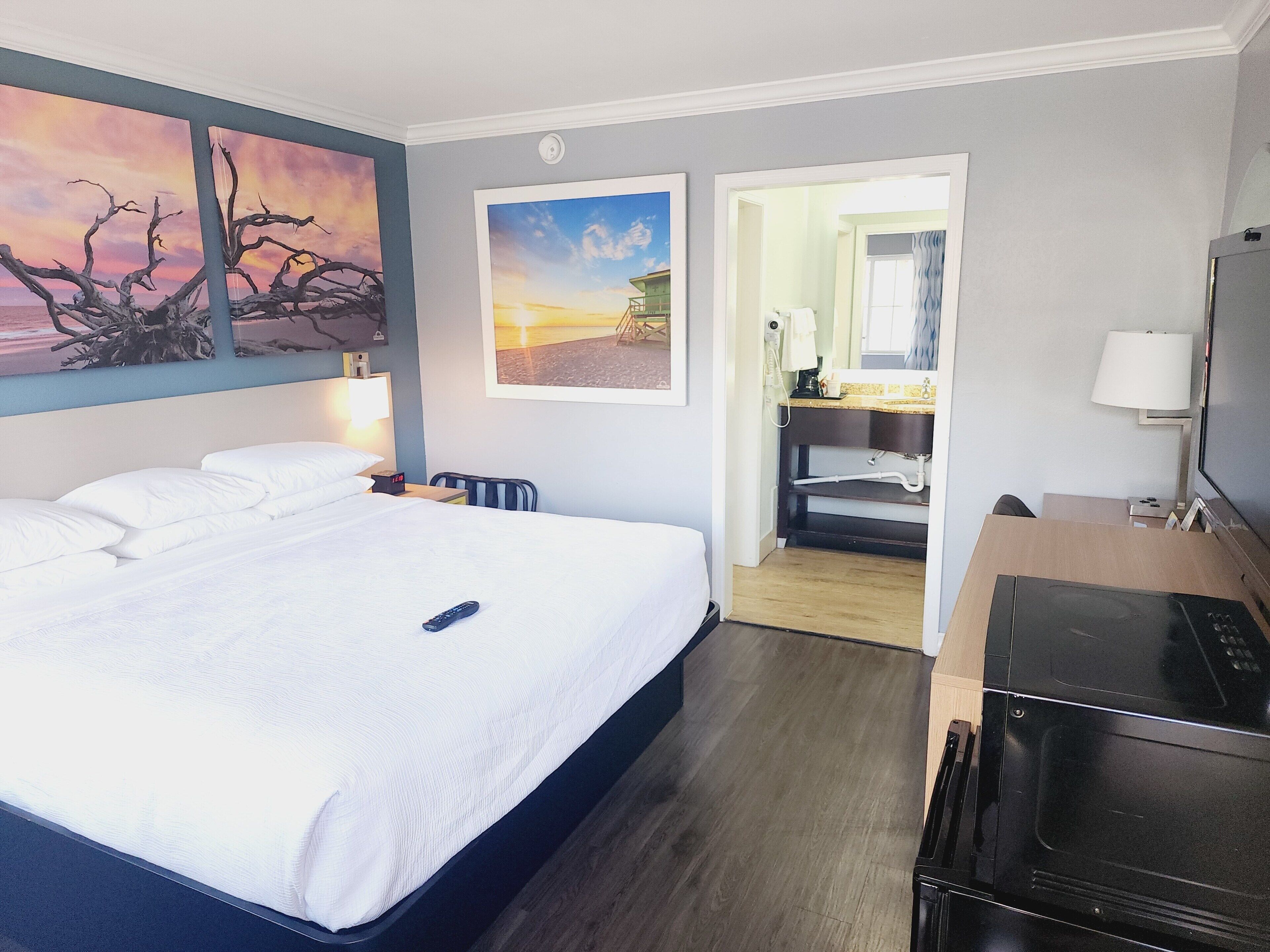 A hotel room with a bed, a desk, a TV, and artwork on the walls.