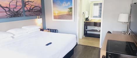 A hotel room with a bed, a desk, a TV, and artwork on the walls.
