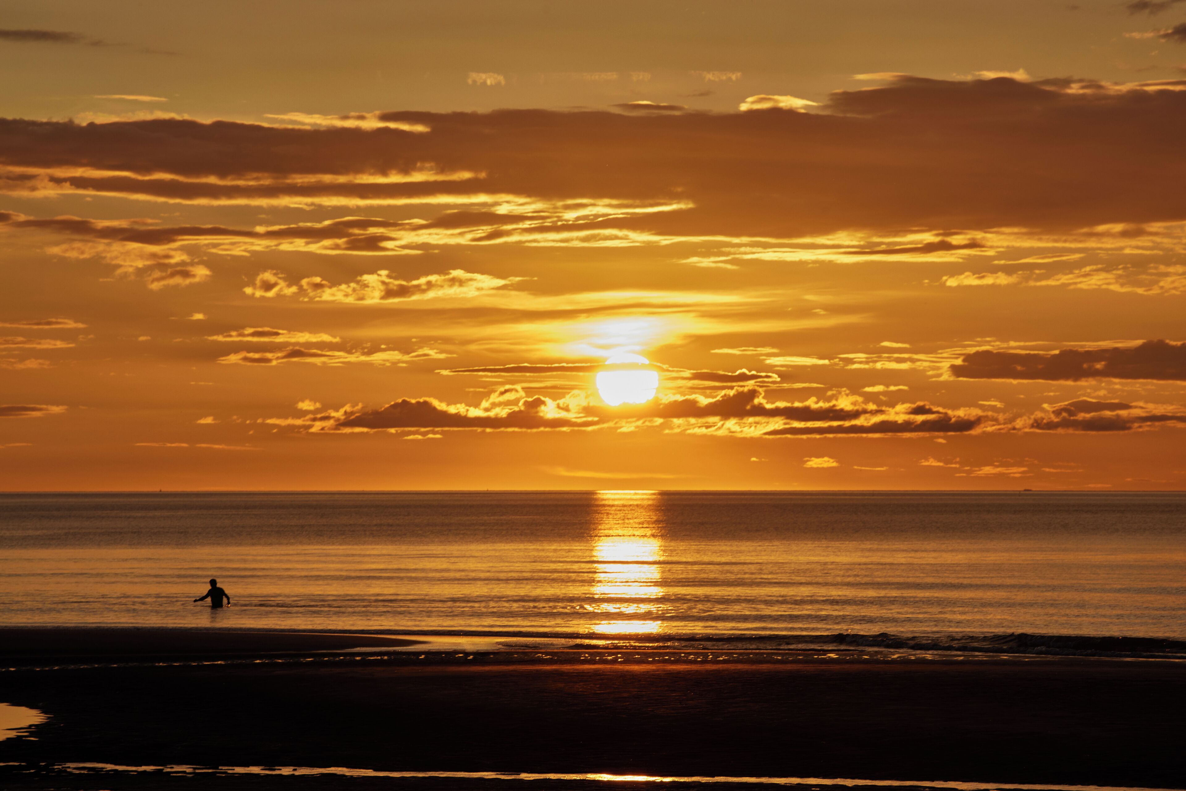 A sunset over a beach with a person walking.