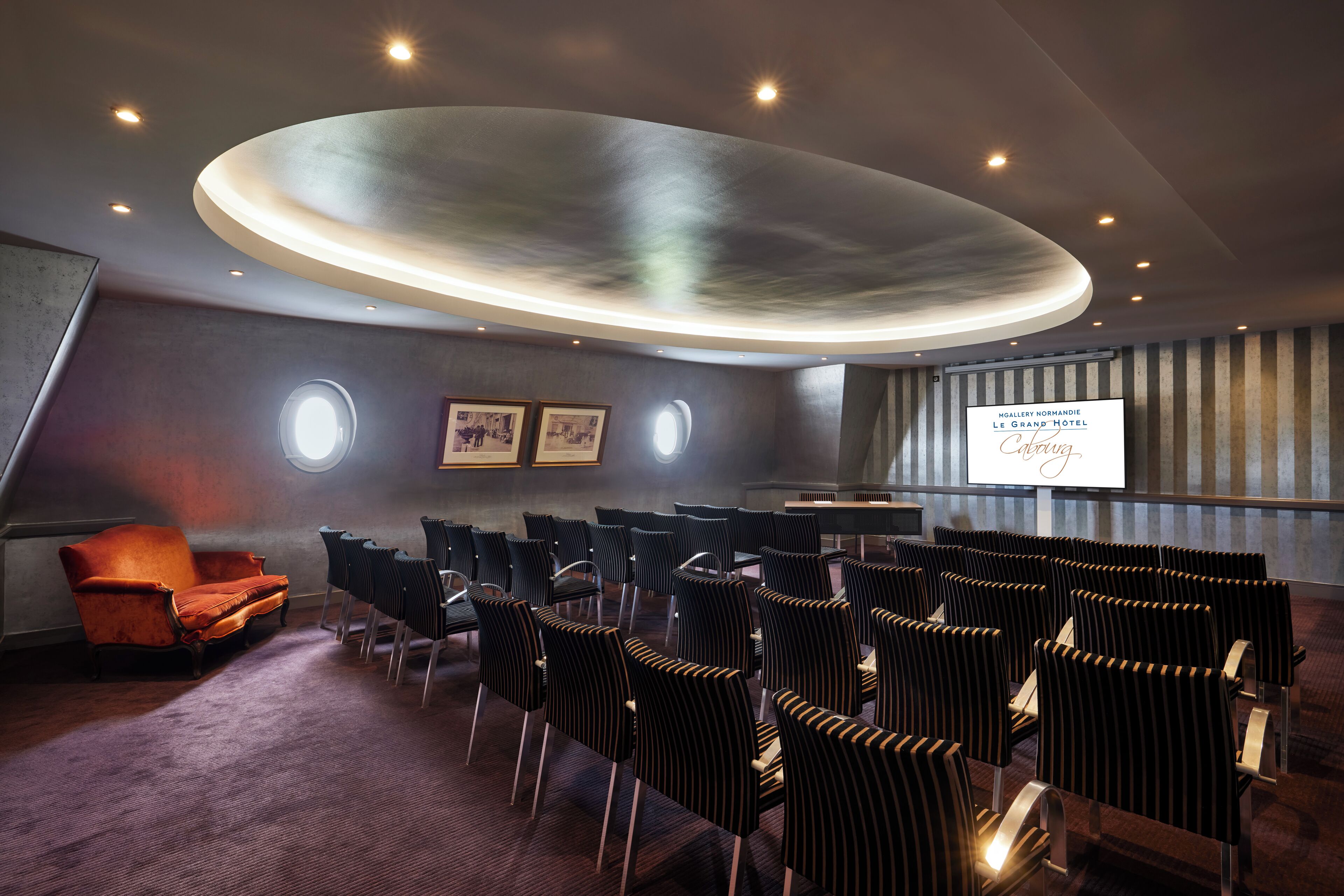 Une salle de conférence dotée d’un plafond au design moderne, d’un pupitre et d’un écran affichant le nom de l’hôtel.
