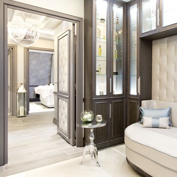 A modern bedroom with a curved sofa, a glass cabinet with toiletries, and a chandelier.