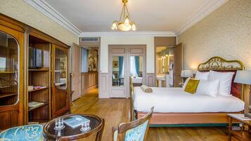 A hotel room with a large bed, a wooden wardrobe, a sitting area with a table and chairs, and a bathroom visible through an open door.
