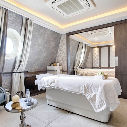 A modern hotel room with a large bed, a sofa, a small round table with a lamp, and a window with curtains.
