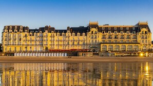 A waterfront hotel with multiple balconies and a reflection in the water. - Le Grand Hotel de Cabourg - MGallery Collection (Cabourg)