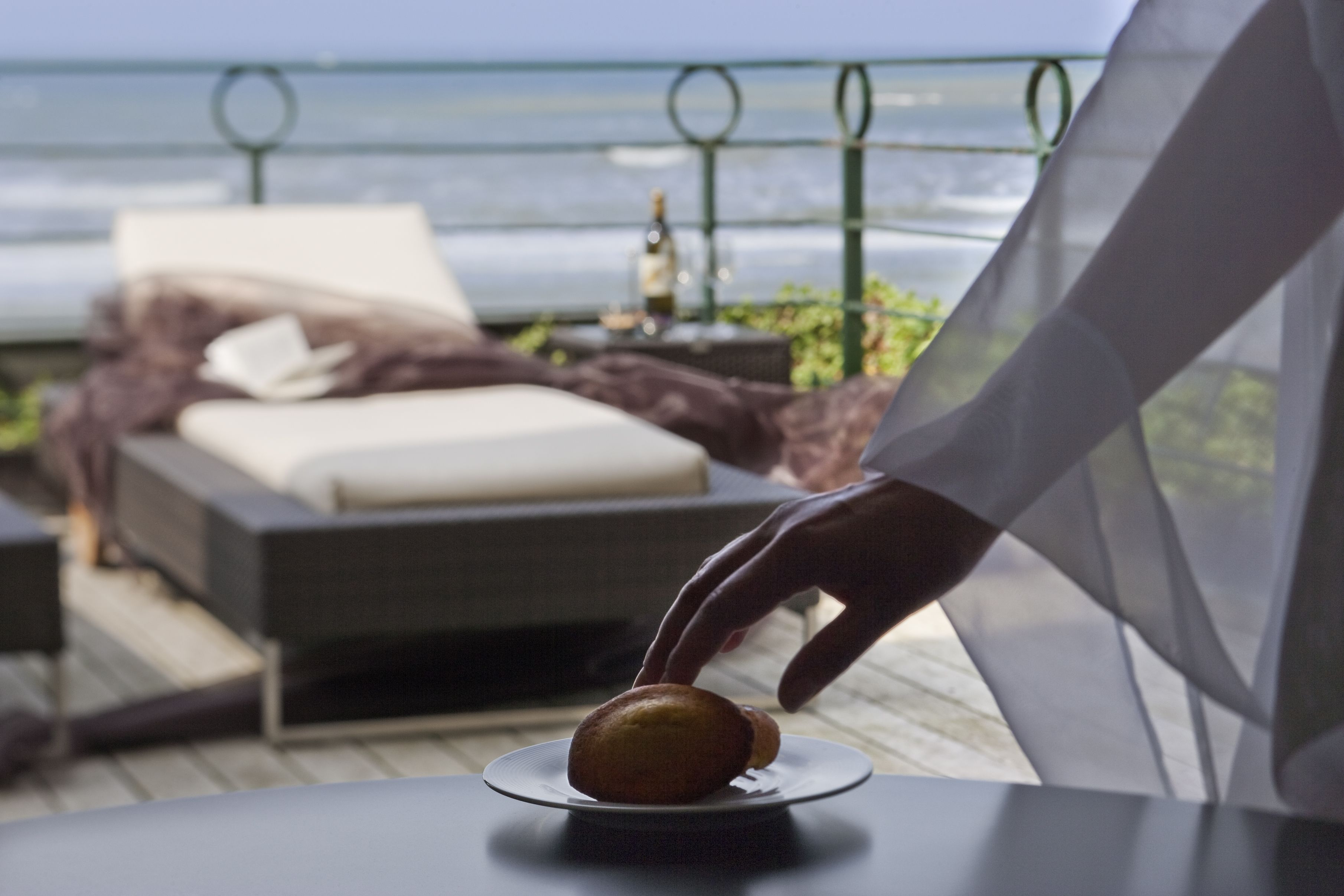 A balcony with a bed, a table with a plate of food, and a bottle.
