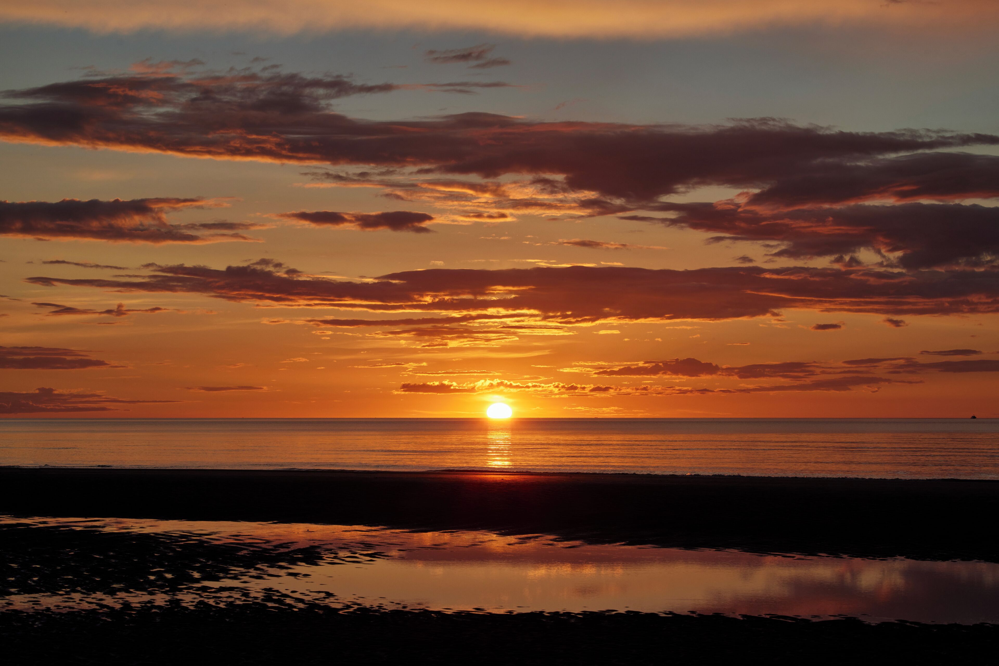 Ein Sonnenuntergang über einem Strand mit ruhigem Wasser, das den Himmel spiegelt.