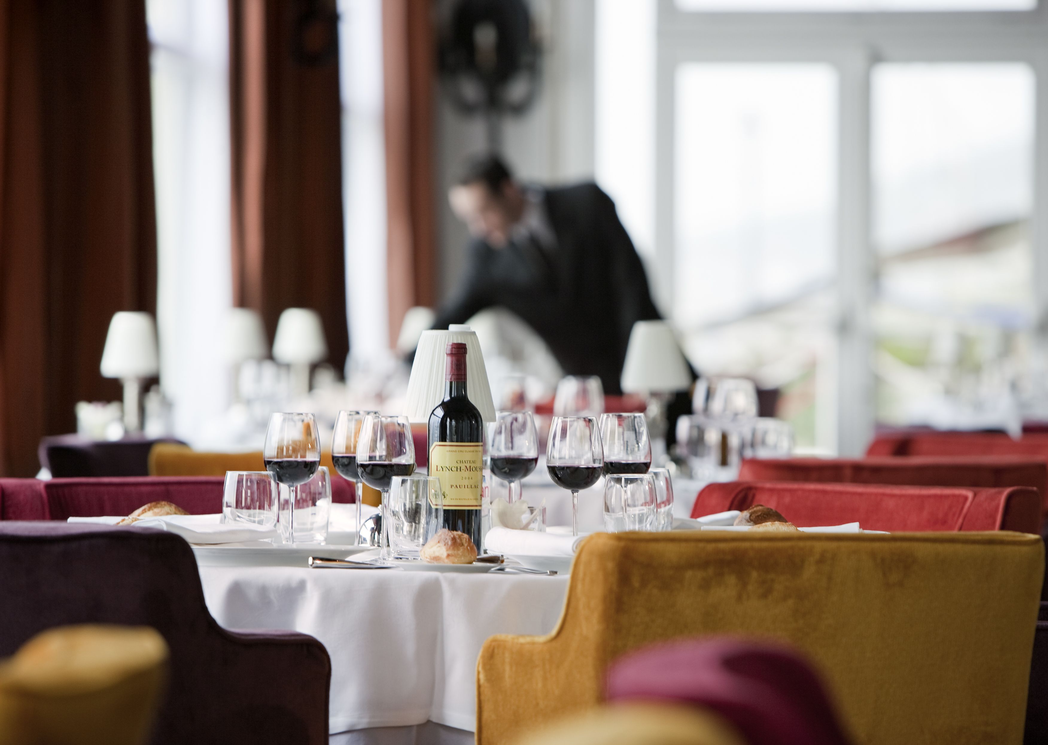 Une salle de restaurant avec des tables dressées pour le dîner, comprenant des verres à vin et une bouteille de vin.