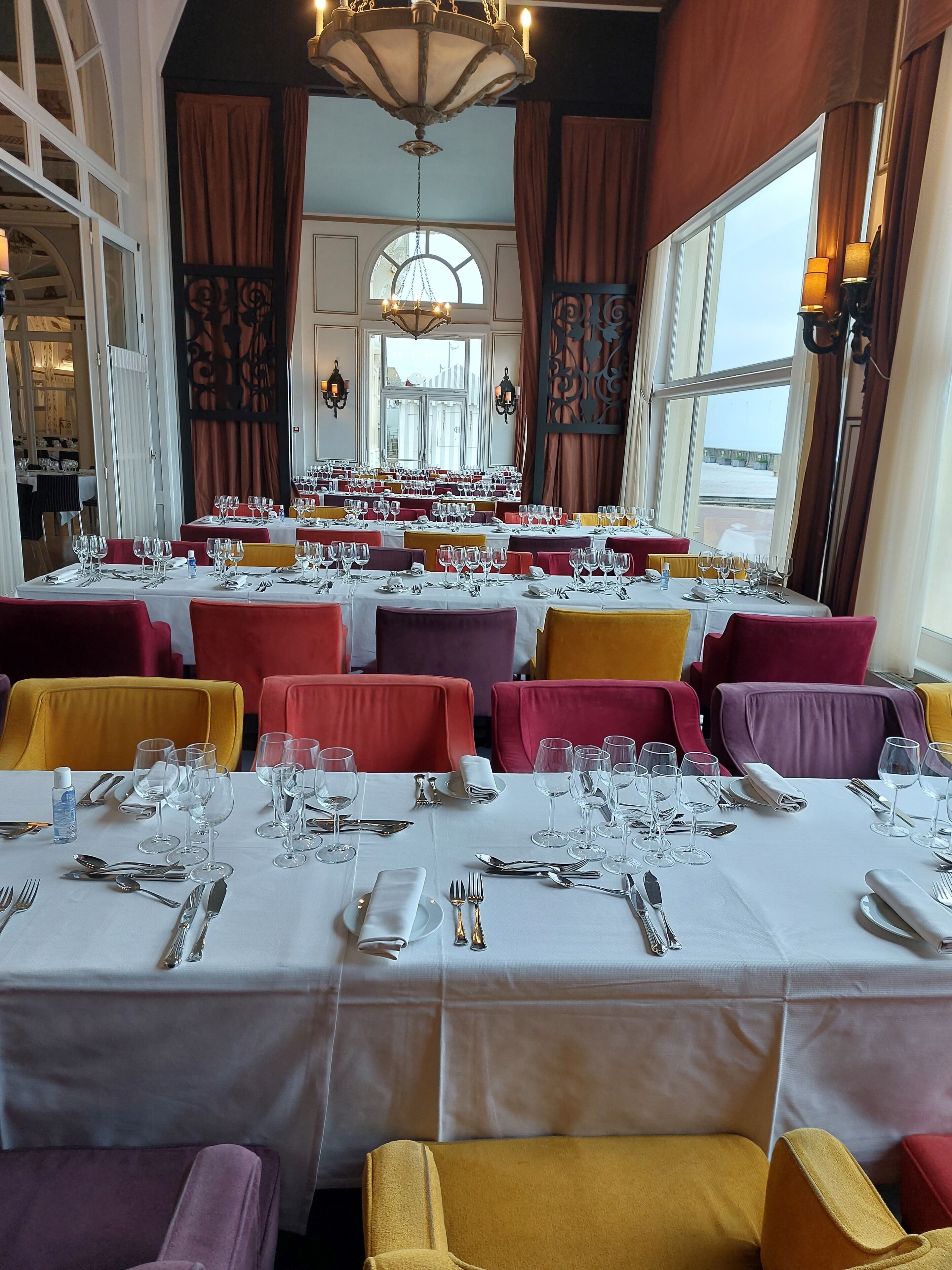 Restaurante com várias mesas preparadas para refeições, apresentando diversas cores de cadeiras e um candelabro.