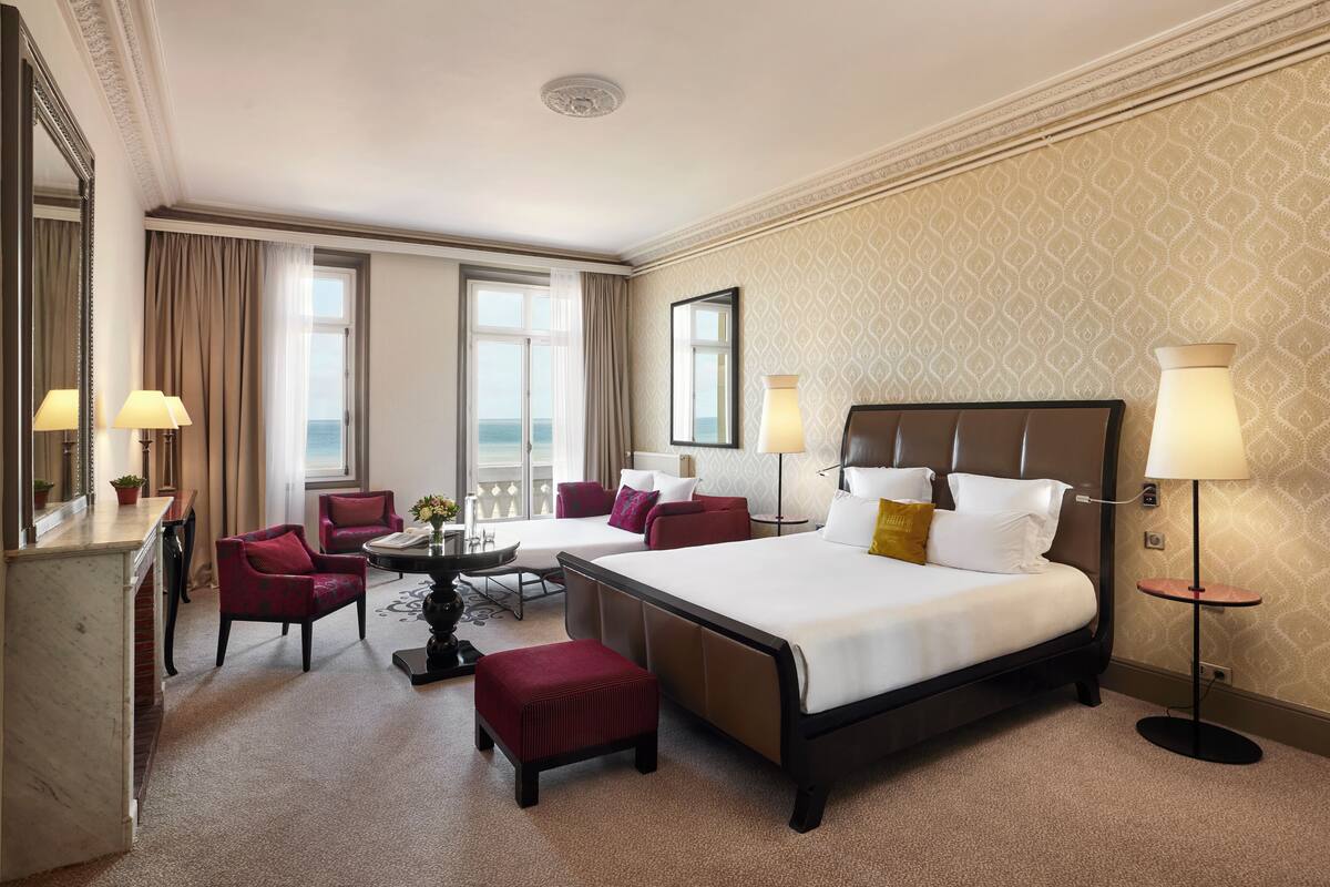 A hotel room with a large bed, two armchairs, a small table, and a desk.