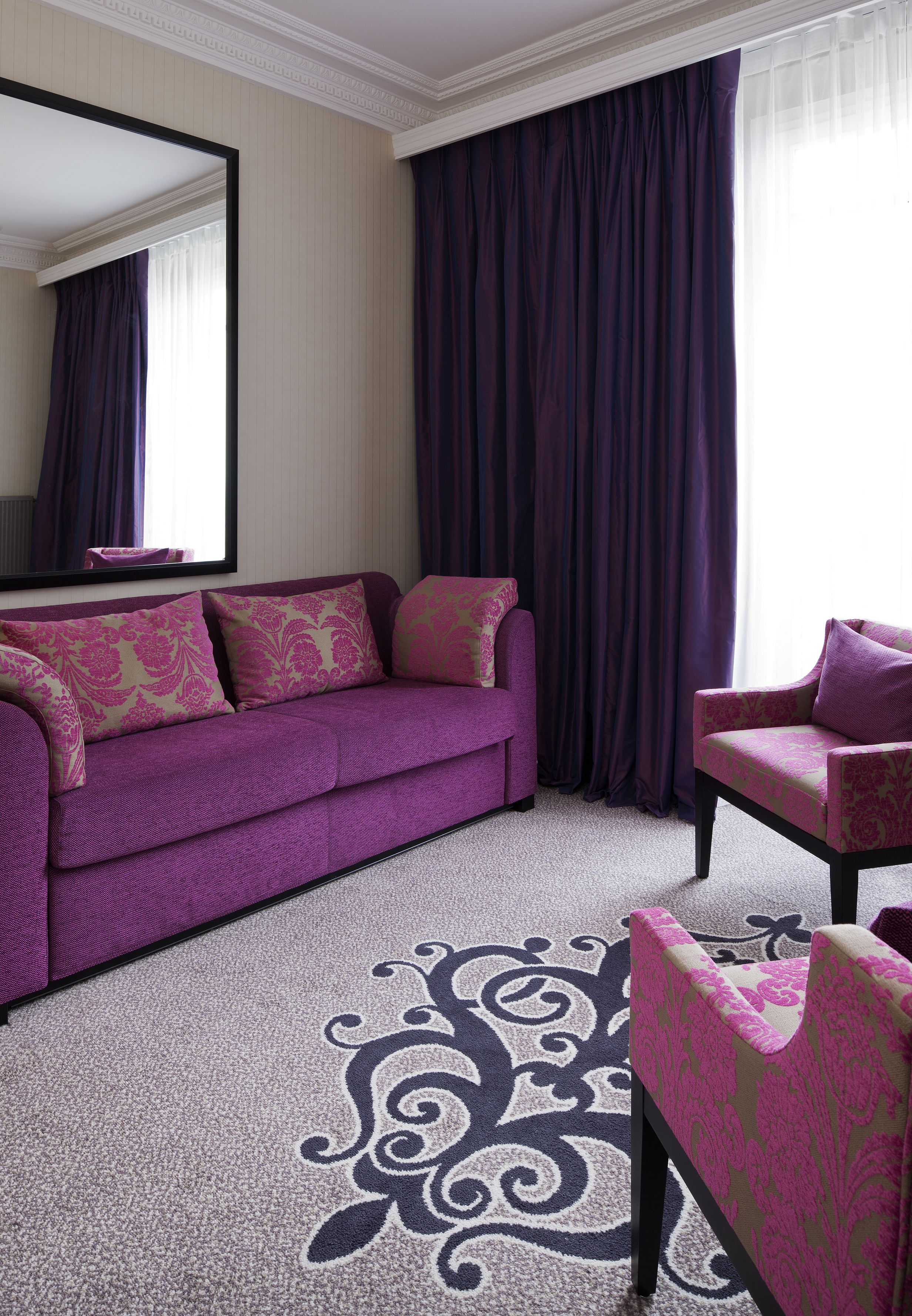 Une pièce avec un canapé violet, un fauteuil assorti et un grand miroir.