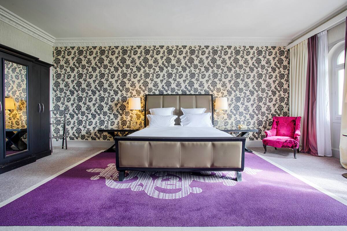 A hotel room with a large bed, a nightstand, a chair, and a wardrobe.