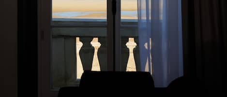 A room with a view of a beach through a window with curtains.