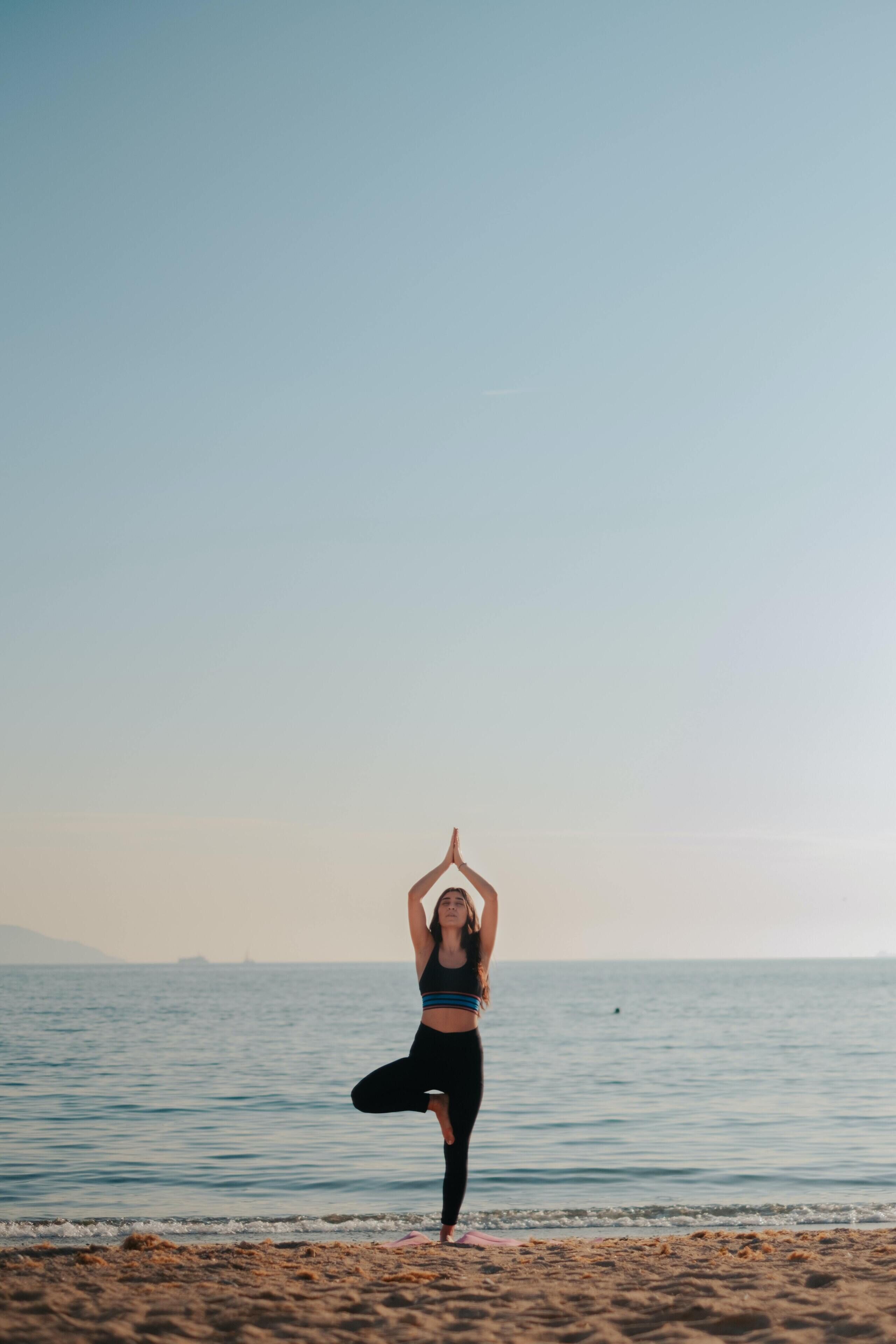 Una persona realizando una postura de yoga en una playa con el océano al fondo.