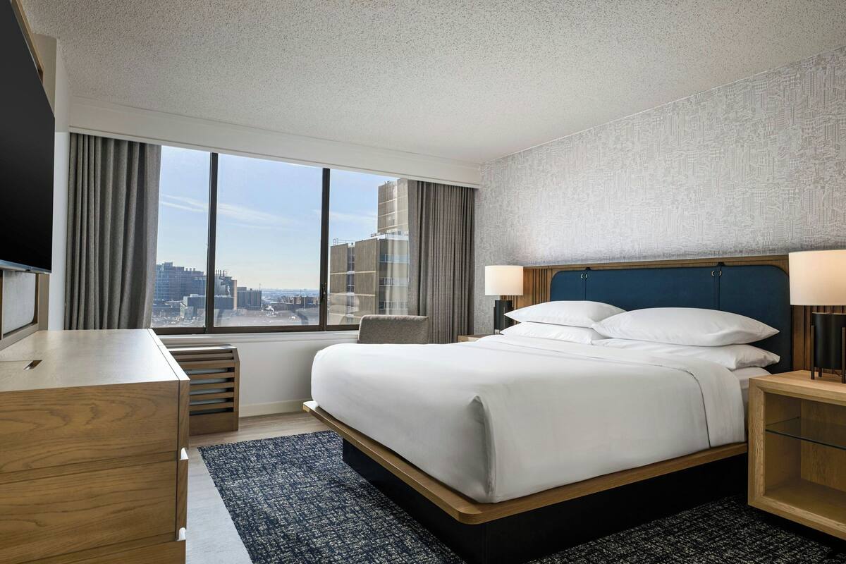 Una habitación de hotel con un ventanal grande, una cama, un escritorio y una silla.