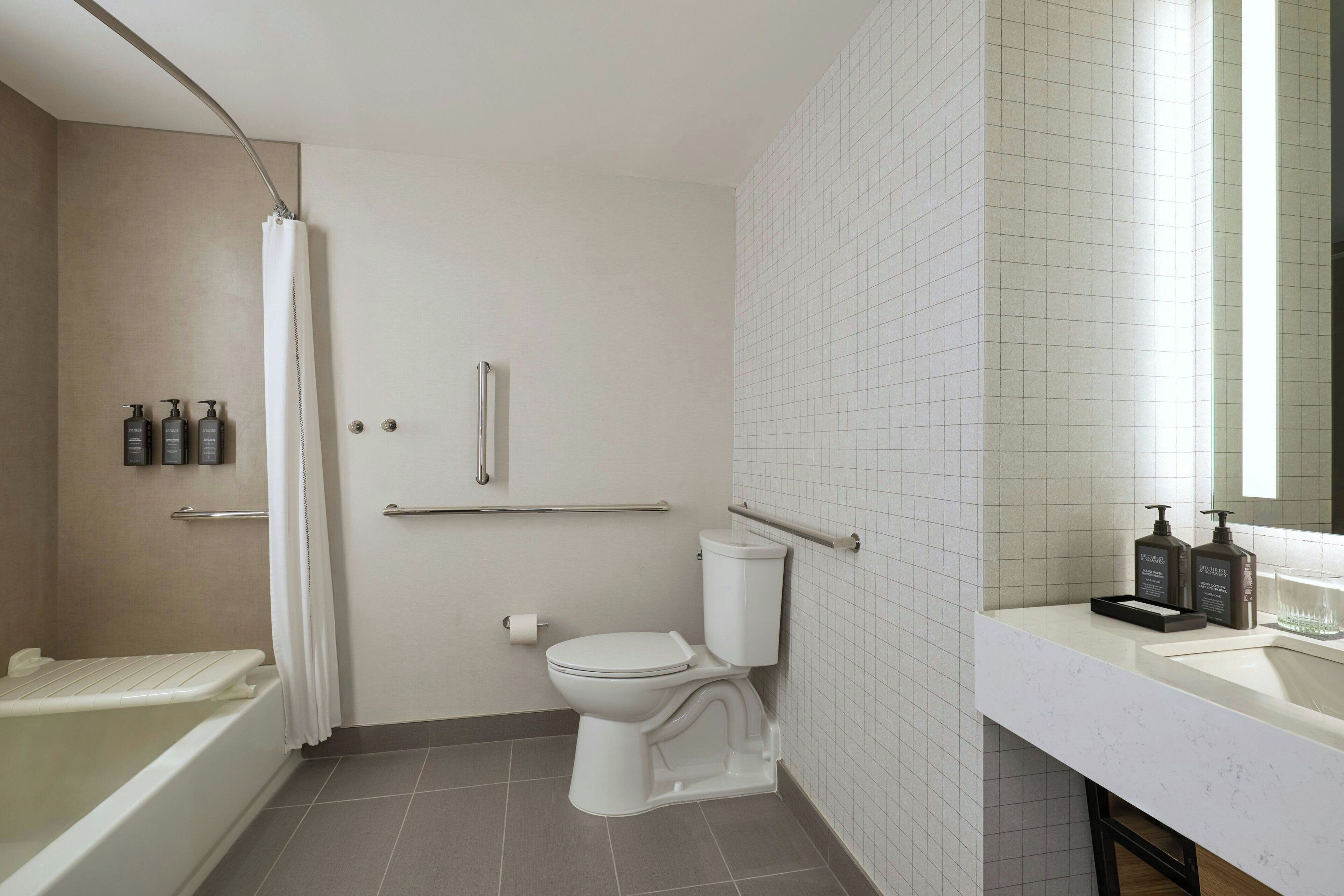Un baño moderno con bañera, inodoro y lavamanos, equipado con barras de apoyo y cortina de ducha.