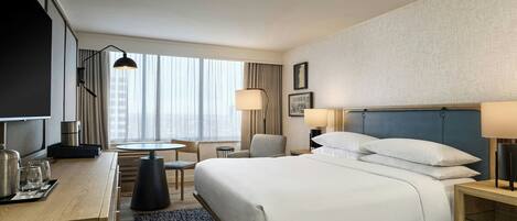 A hotel room with a bed, bedside tables, a desk, a chair, a TV, and a window with curtains.