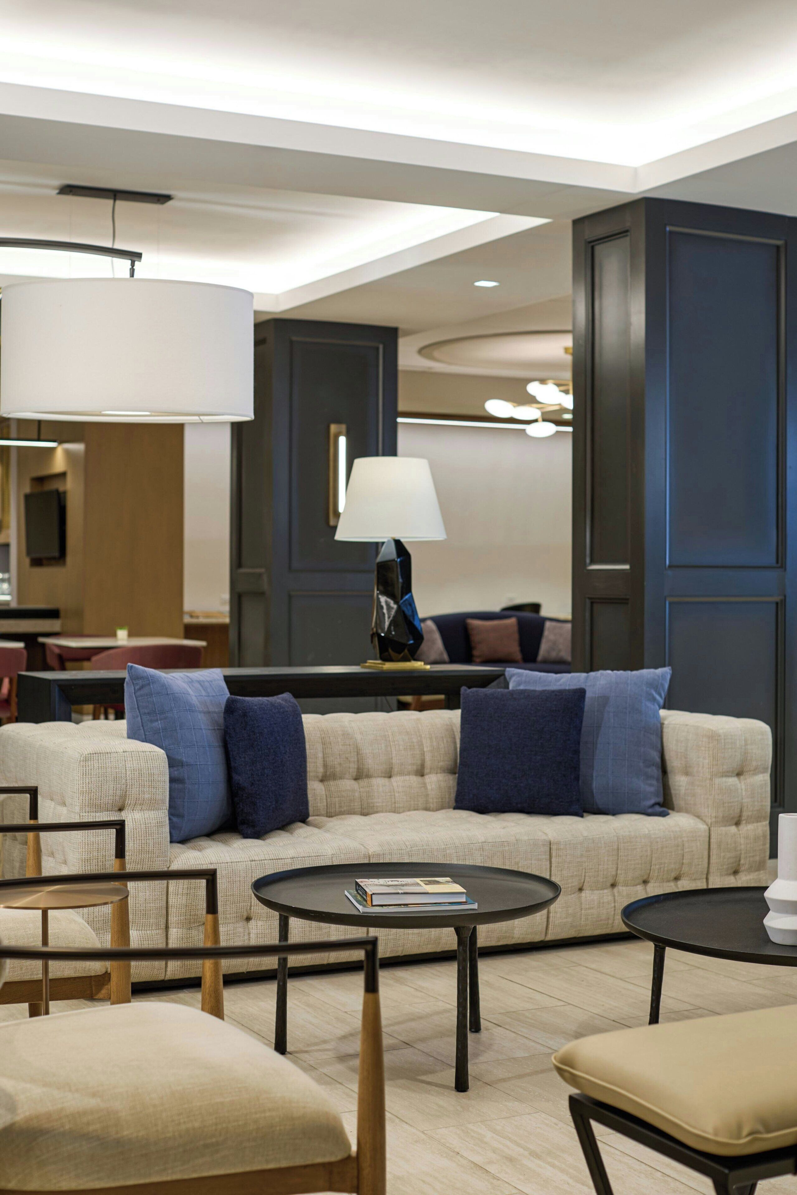 A modern hotel room with a sofa, two side tables, a lamp, and a television.