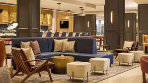 A modern lobby with a sectional sofa, armchairs, ottomans, a coffee table, and a bar area with a television. - Sheraton Philadelphia University City Hotel (Philadelphia)
