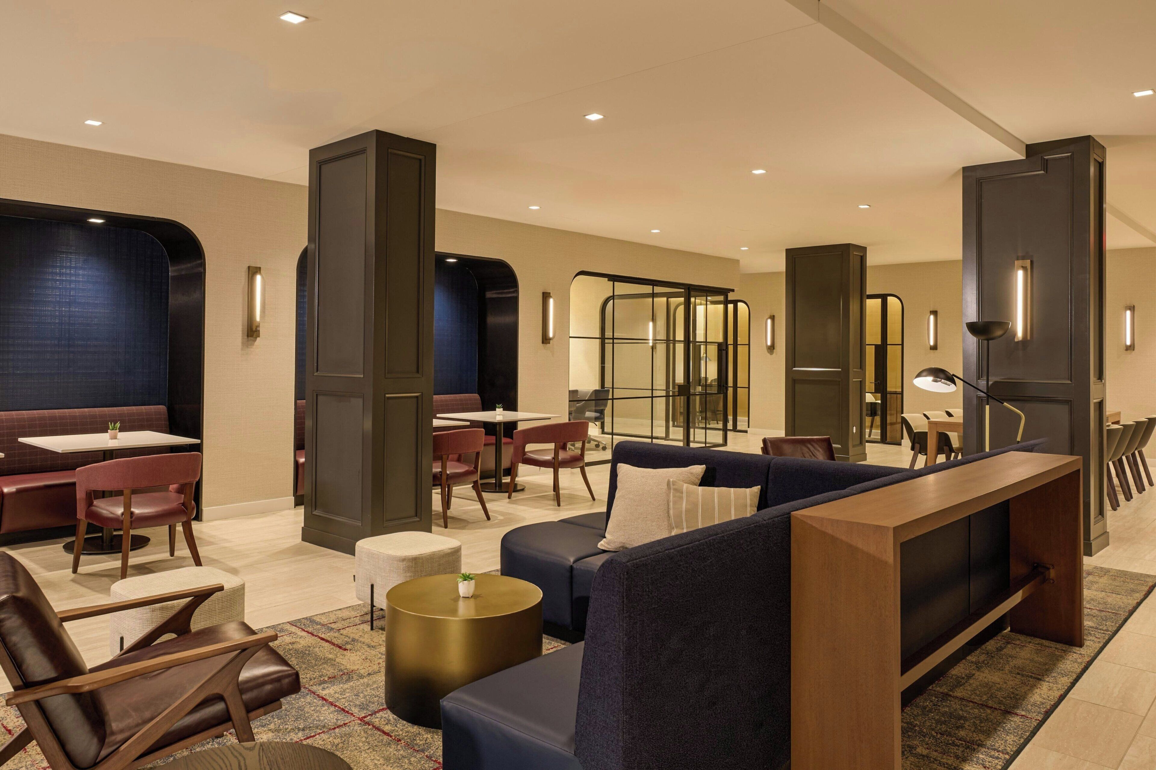 A modern hotel lobby with seating areas, a reception desk, and a large mirror.