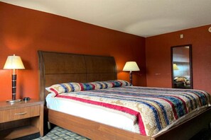 A single bed with a wooden headboard, two bedside lamps, a mirror on the wall, and a small wooden nightstand. - Real Value Inn (Memphis)