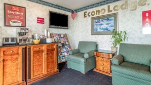 A room with a kitchenette, a television, a green armchair, a sofa, and a wall with the text "Econo Lodge." - Econo Lodge Castro Valley I-580 (Castro Valley)