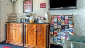 A hotel room with a wooden cabinet, a coffee station, a TV mounted on the wall, and a wall display of various travel brochures. - Econo Lodge Castro Valley I-580 (Castro Valley)