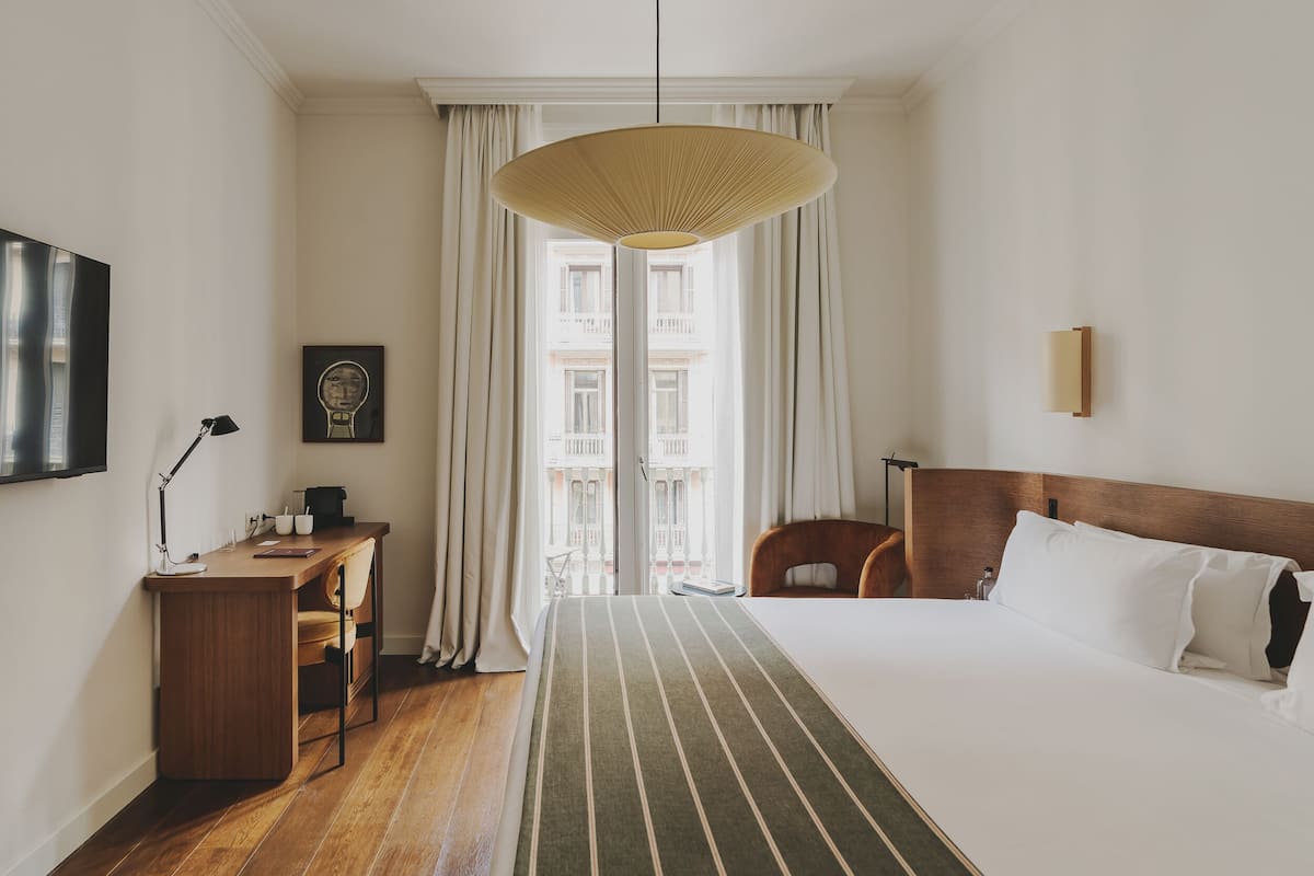A hotel room with a bed, a desk, a chair, a television, and a window with curtains.
