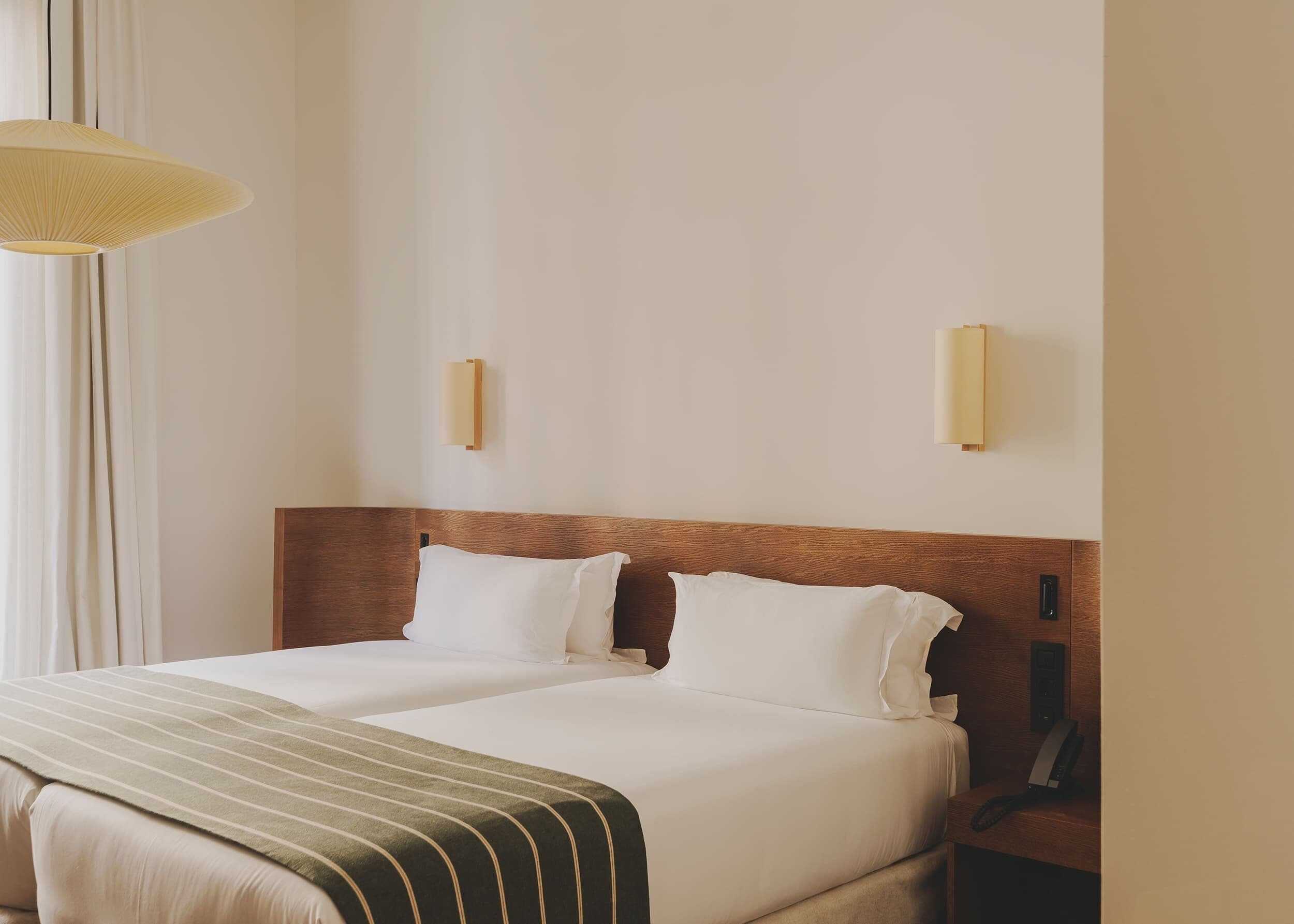 Un lit double avec une tête de lit en bois, deux tables de chevet, un téléphone et un luminaire fixé au mur.