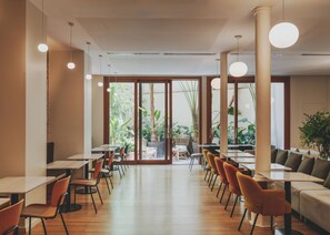 Moderni ravintola, jossa on pitkä tiski, useita pöytiä ja tuoleja. Suurista ikkunoista avautuu näkymä vehreään maisemaan.