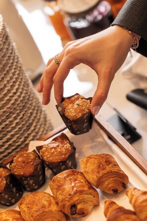 A hand holding a chocolate-covered pastry with a visible 'P' logo, surrounded by other pastries on a tray. - Hotel Regina Barcelona (Barcelona)