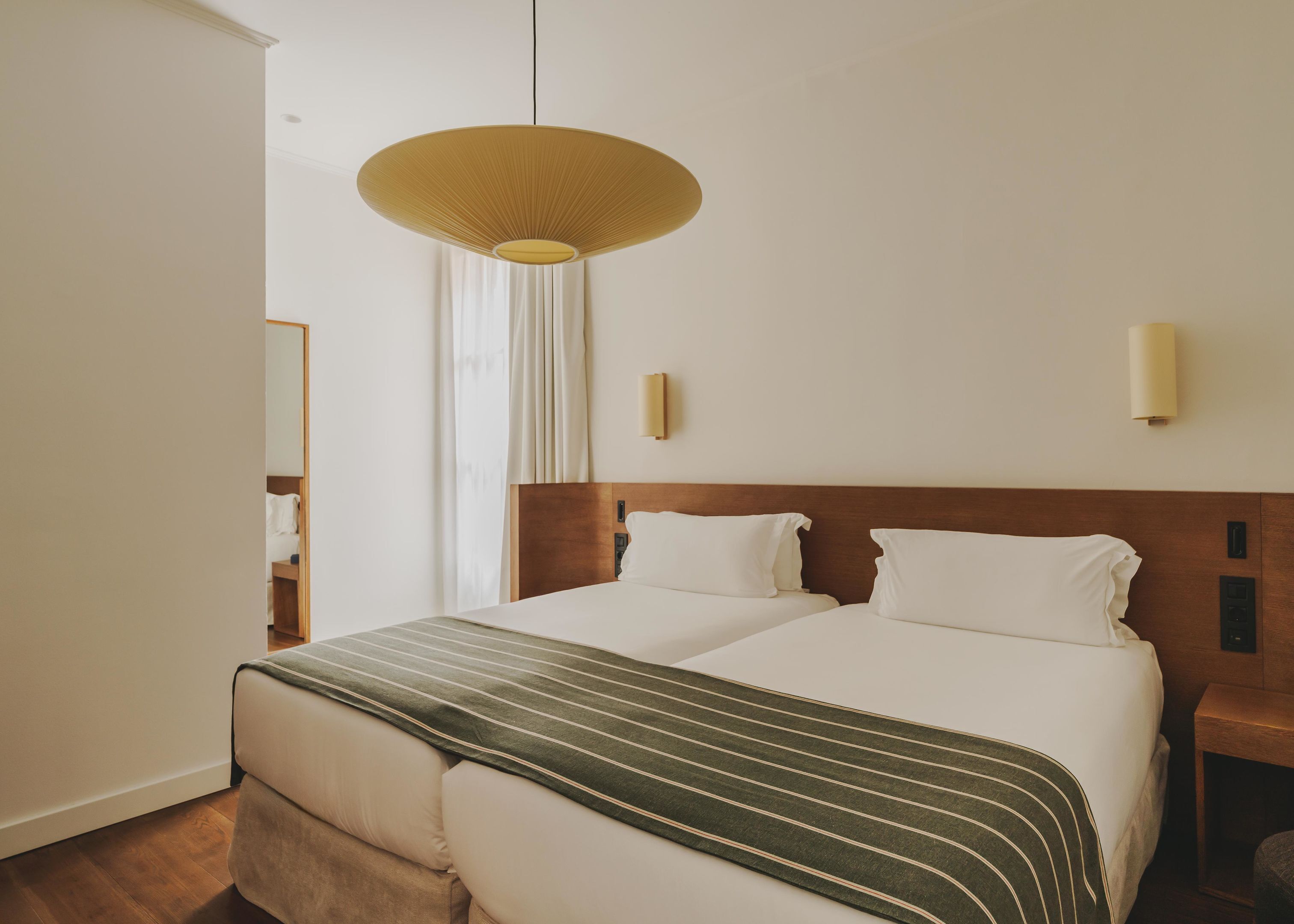 Habitación de hotel con una cama grande, un cabecero de madera, una lámpara colgante y una mesita de noche con lámpara.