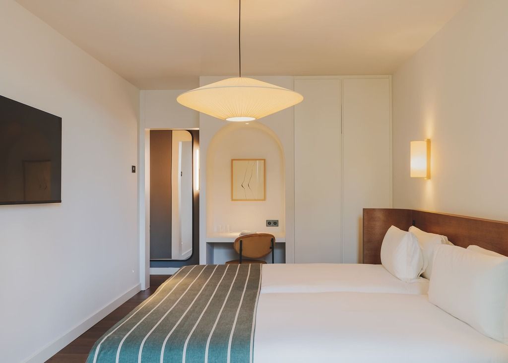 A hotel room with a bed, a bedside table, a chair, a wall-mounted TV, and a pendant light.