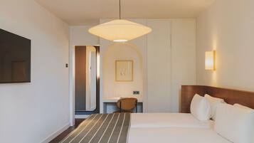 A hotel room with a bed, a bedside table, a chair, a wall-mounted TV, and a pendant light.