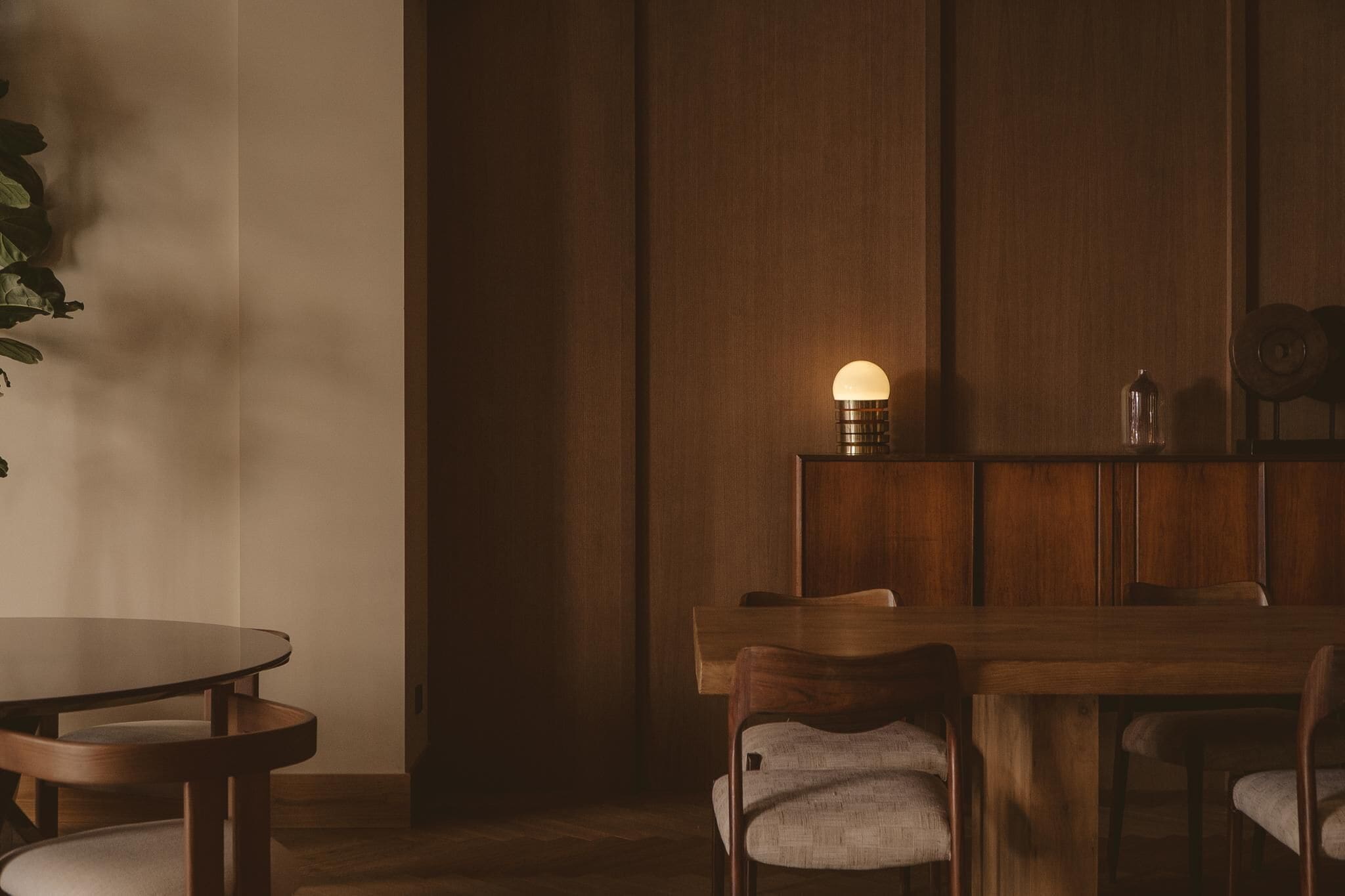 Una mesa de madera con sillas, una lámpara fijada a la pared y una planta en maceta.