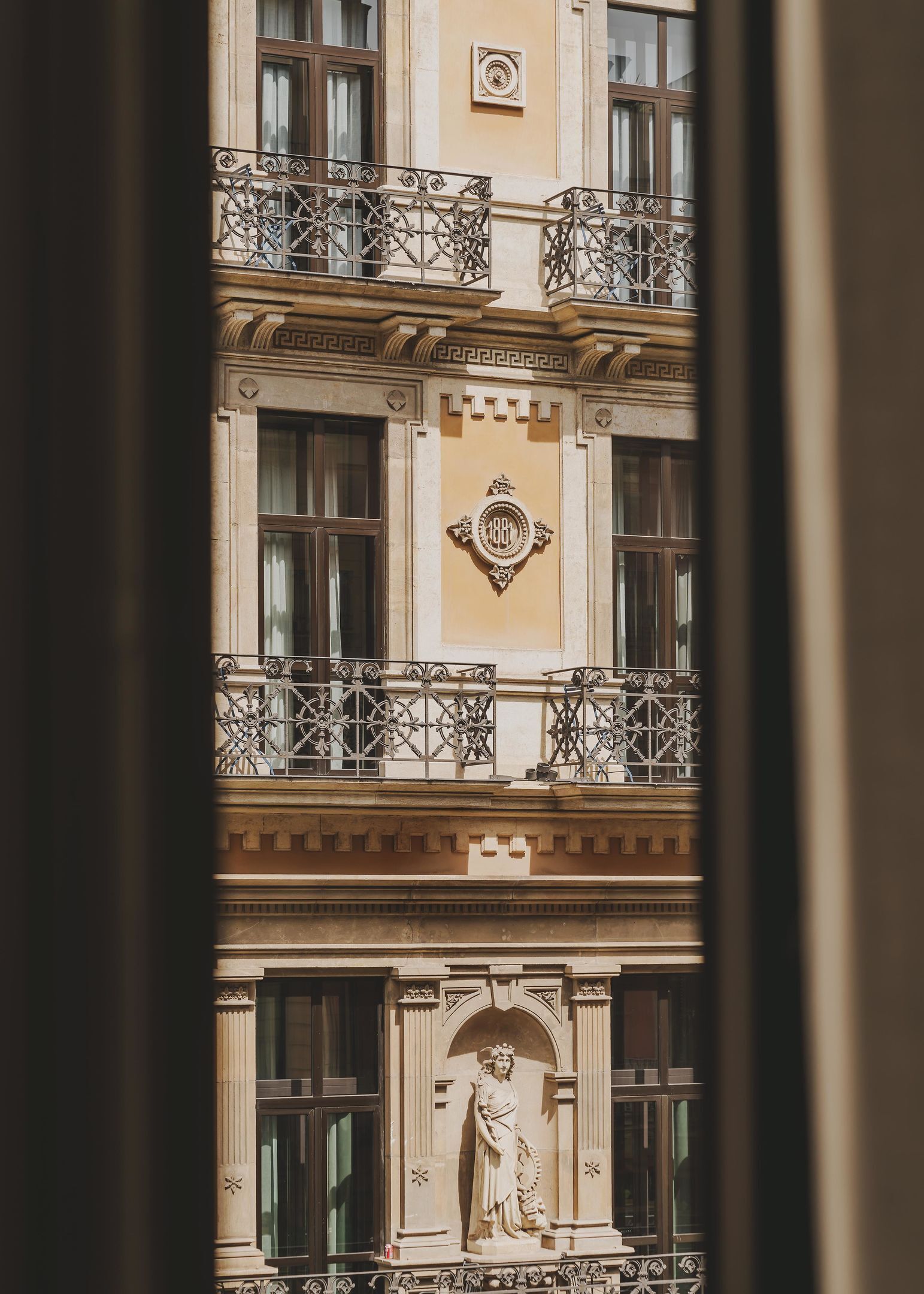 A building facade with ornate balconies, a central plaque, and a statue below the windows.