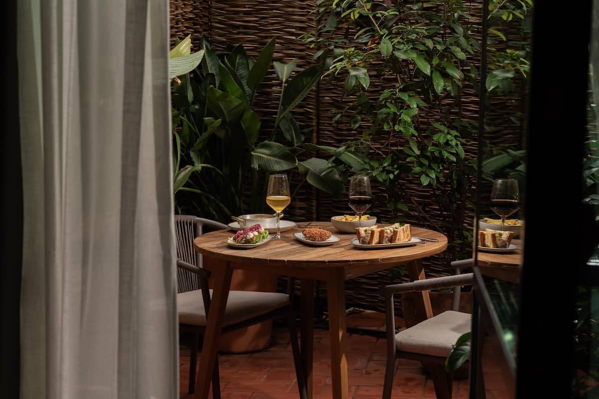 A round wooden table set with plates of food, glasses of wine, and a wicker backdrop.