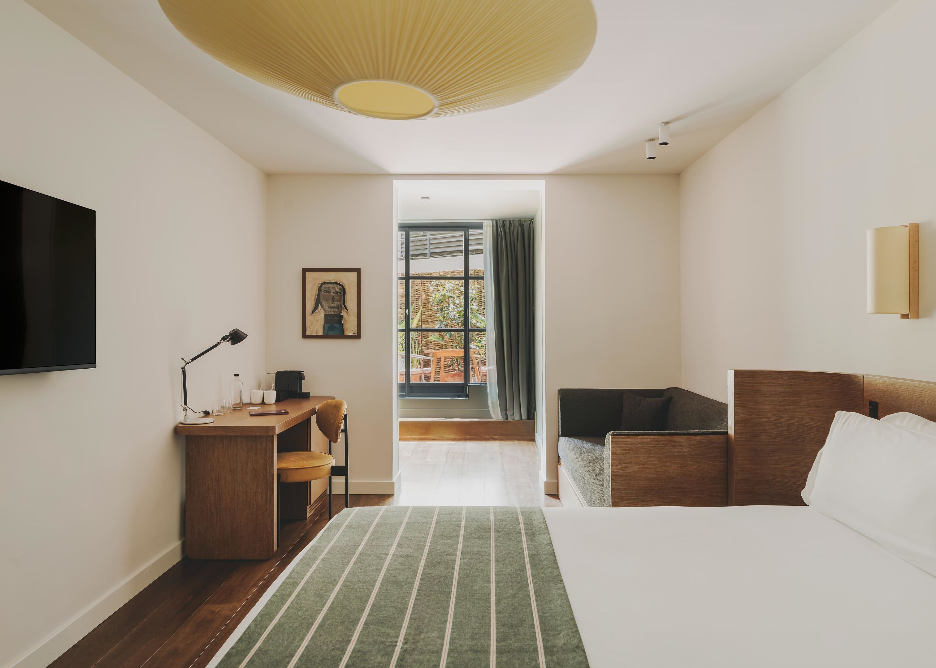A modern hotel room with a large bed, a desk with a chair, a sofa, and a television on the wall.