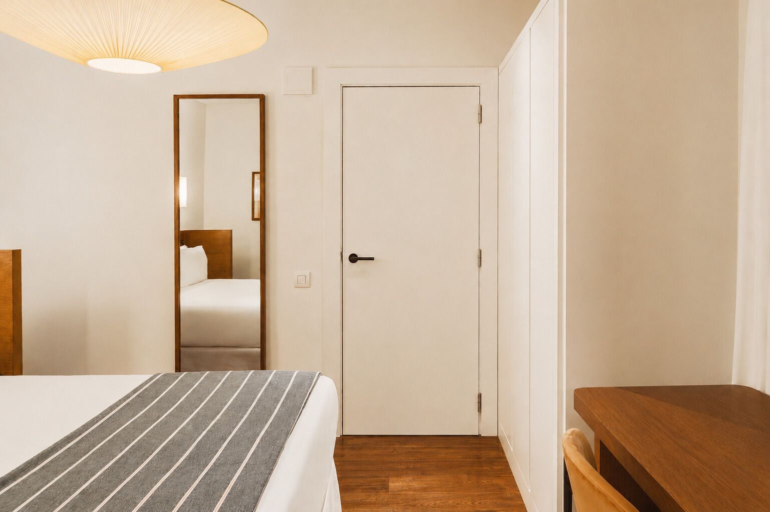 Una habitación de hotel con una cama, una mesita de noche de madera, una puerta y un espejo.