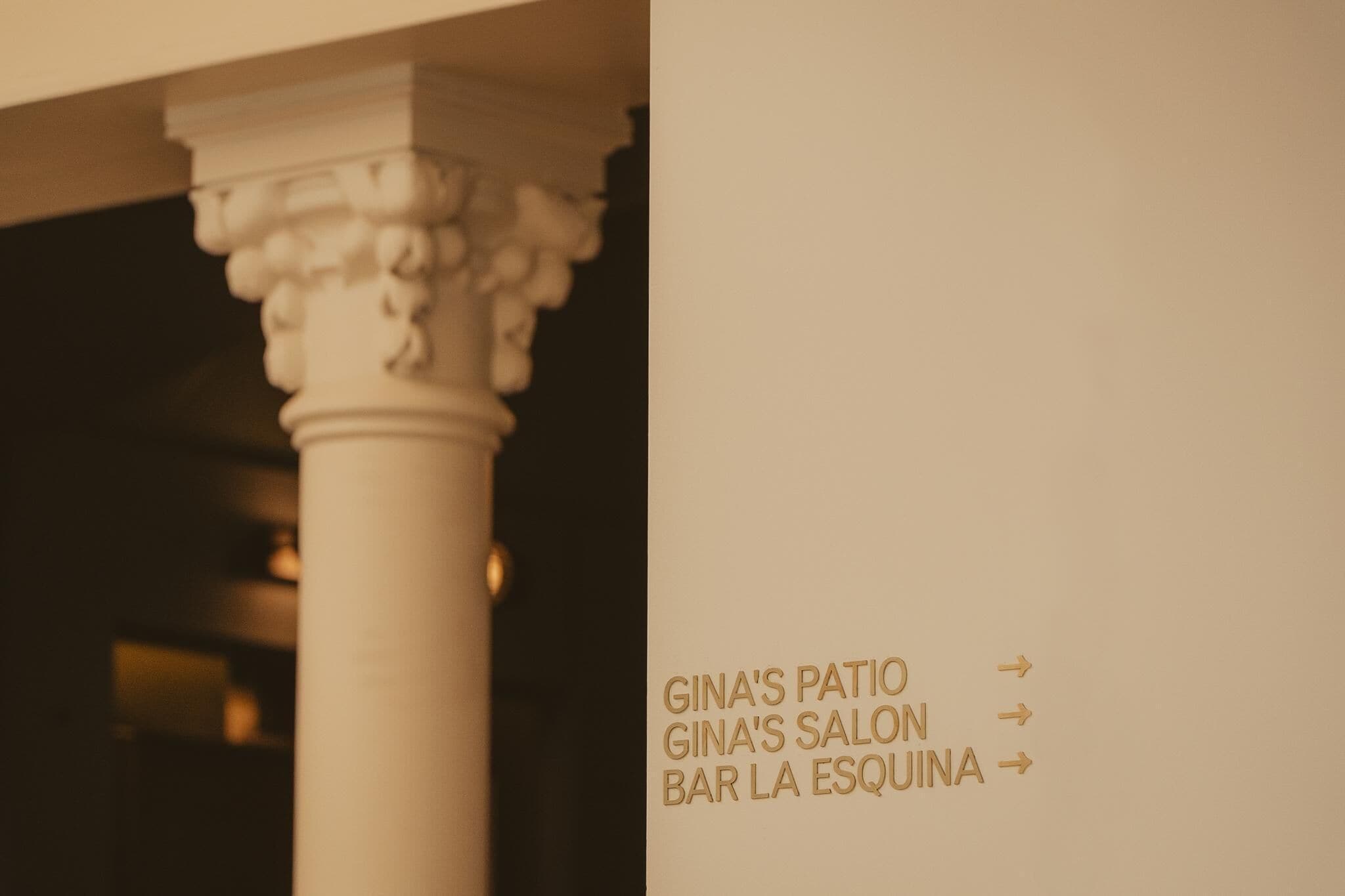 A column with a sign indicating directions to GINA'S PATIO, GINA'S SALON, and BAR LA ESQUINA.